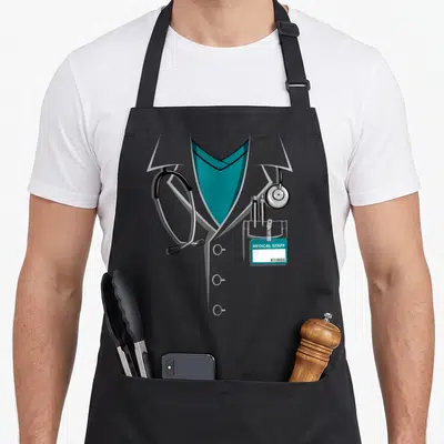 Lab halloween apron - Cartoon grey doctor coat with teal V-neck, stethoscope, two pens, and medical staff ID badge — shown on a black cotton canvas apron against a white background