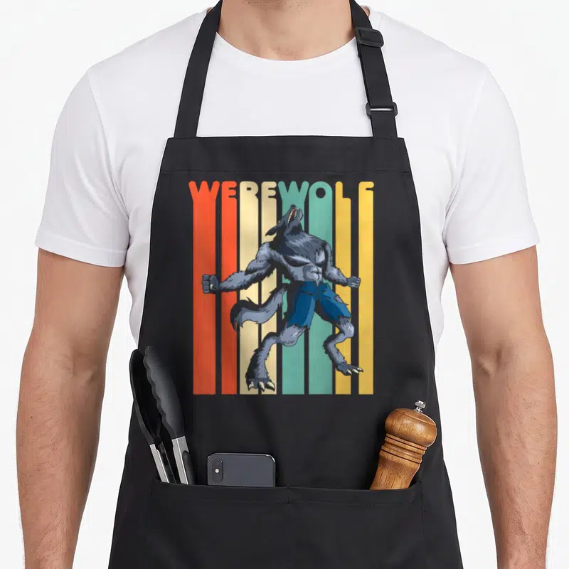 Werewolf halloween apron - Grey werewolf standing before red orange yellow and blue vertical stripes with WEREWOLF text — shown on a black cotton canvas apron against a white background