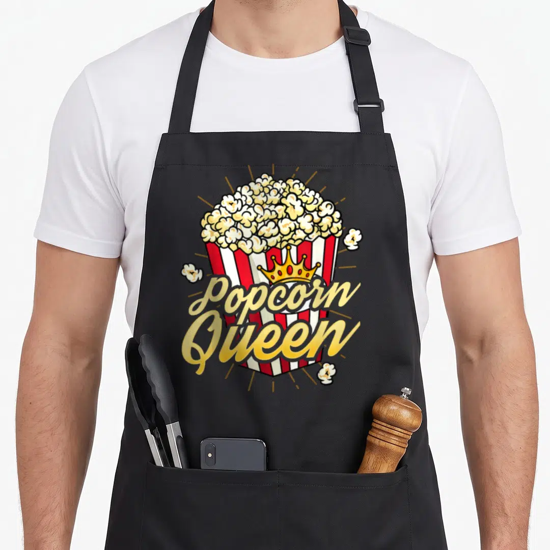 Movie popcorn apron - Red and white striped bucket with yellow crown and script text 'Popcorn Queen' — shown on a black cotton canvas apron against a white background