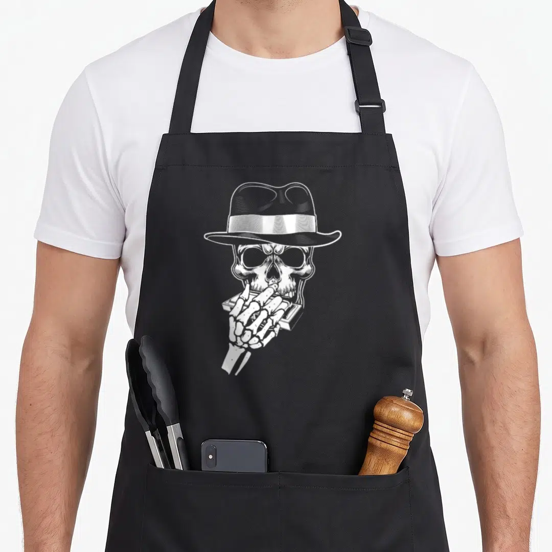 Harmonica skeleton apron - White line-art skull in fedora holding a harmonica on black fabric — shown on a black cotton canvas apron against a white background