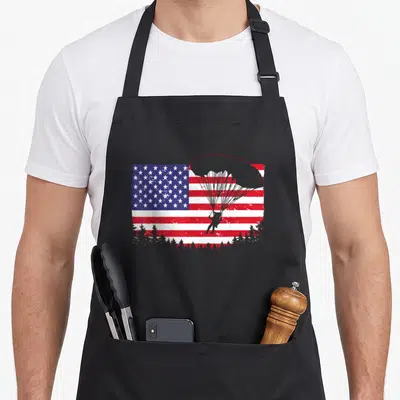 Skydiving american flag apron - Distressed American flag with red parachute outline and grey paratrooper silhouette — shown on a black cotton canvas apron against a white background