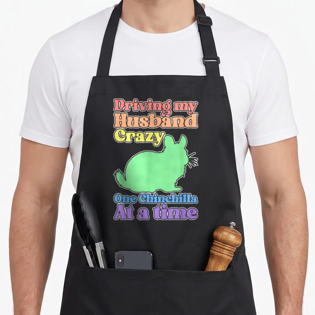 Chinchilla driving apron - Green chinchilla silhouette with rainbow stacked text reading Driving my Husband Crazy One — shown on a black cotton canvas apron against a white background