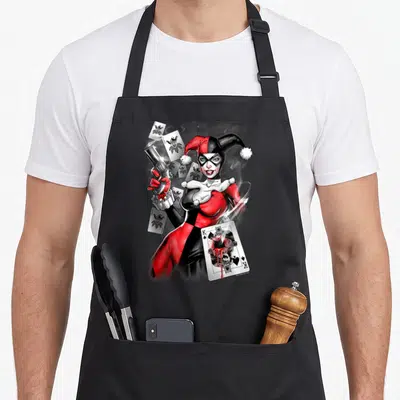 Gun vehicle apron - Harley Quinn holding gun surrounded by jokers and damaged Batman king card in red black white — shown on a black cotton canvas apron against a white background