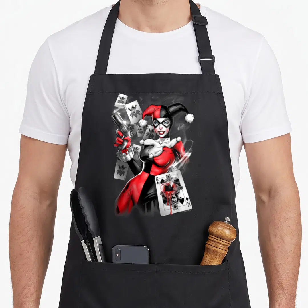 Gun vehicle apron - Harley Quinn holding gun surrounded by jokers and damaged Batman king card in red black white — shown on a black cotton canvas apron against a white background