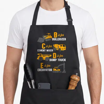 Construction heavy canvas aprons - B is for BULLDOZER, C is for CEMENT MIXER, D is for DUMP TRUCK, E is for EXCAVATOR — shown on a black cotton canvas apron against a white background