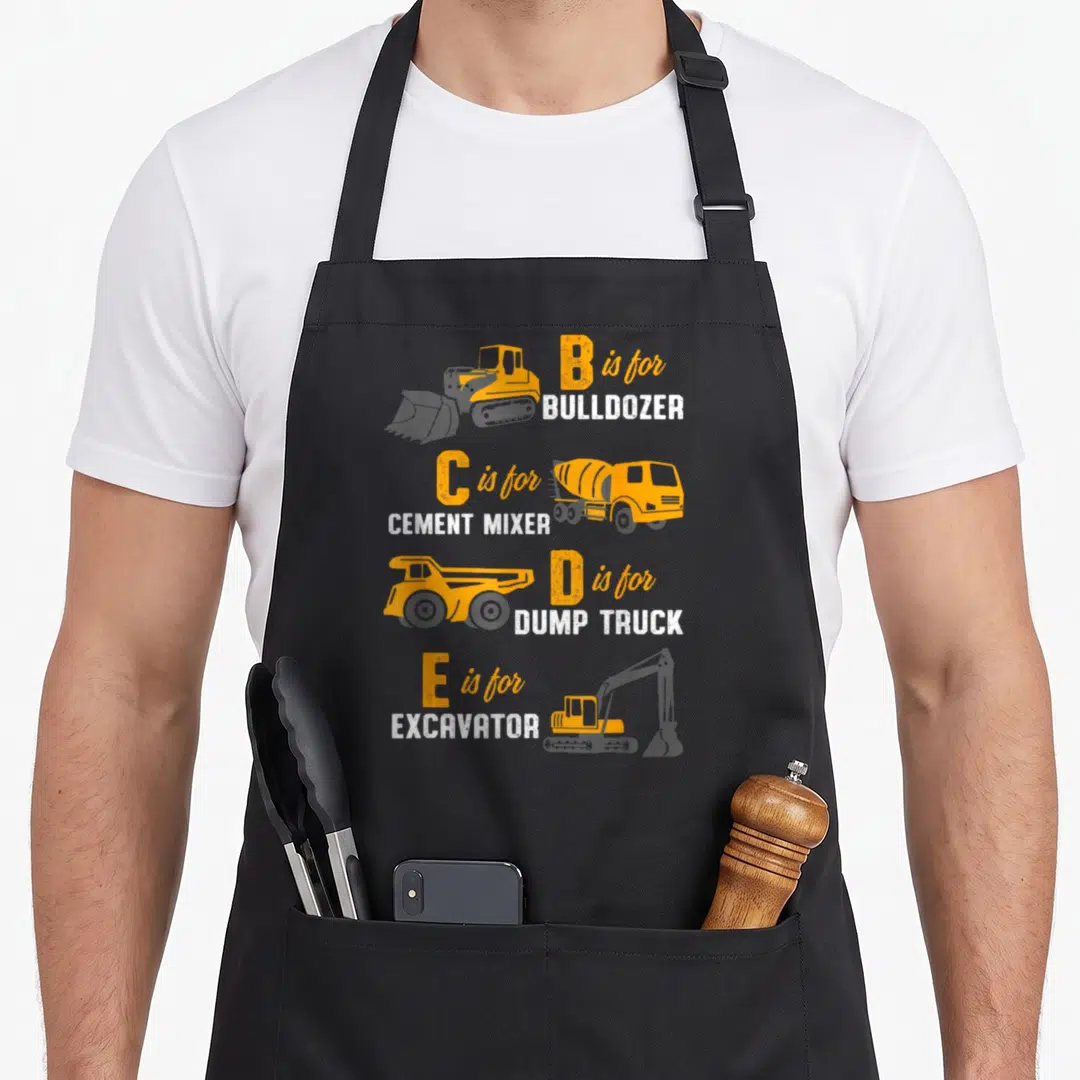 Construction heavy canvas aprons - B is for BULLDOZER, C is for CEMENT MIXER, D is for DUMP TRUCK, E is for EXCAVATOR — shown on a black cotton canvas apron against a white background