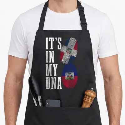 Haiti dominican pride apron - IT'S IN MY DNA text beside two fingerprints filled with Dominican and Haitian flags — shown on a black cotton canvas apron against a white background