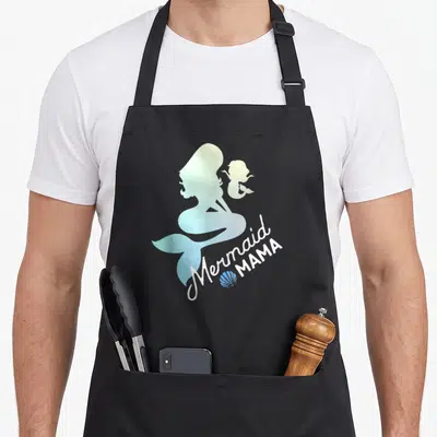 Sea mama apron - Blue and white mermaid silhouettes with text and seashell graphic — shown on a black cotton canvas apron against a white background