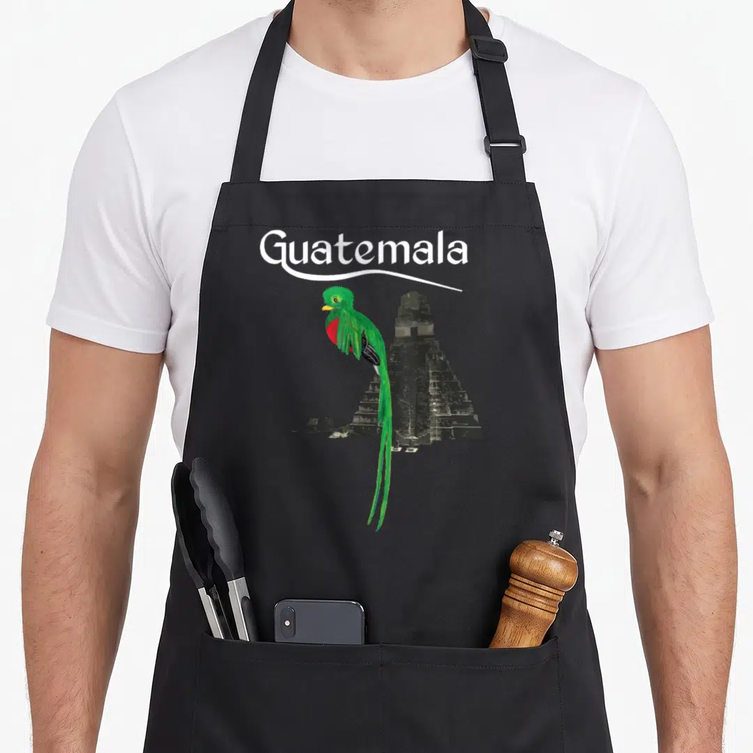Chapin antigua guatemala apron - Green quetzal bird perched before a Mayan pyramid under white Guatemala text — shown on a black cotton canvas apron against a white background