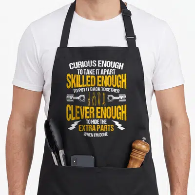 Tool car apron - Stacked yellow and white text with pistons, screwdriver, pliers, wrenches, and lightning bolts — shown on a black cotton canvas apron against a white background