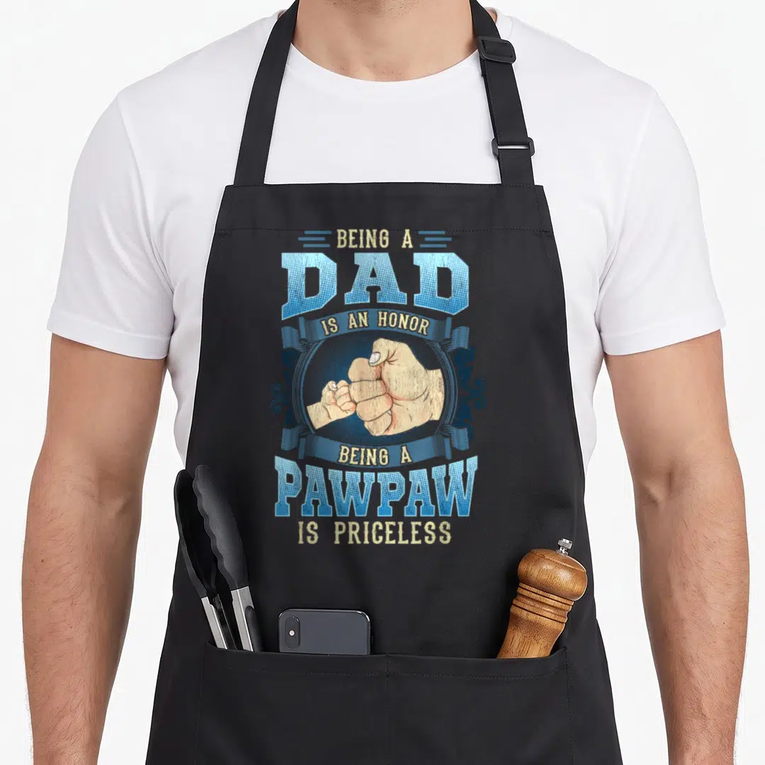 Honor papaya apron - Retro blue and beige fist bump graphic with text about being a dad and pawpaw — shown on a black cotton canvas apron against a white background
