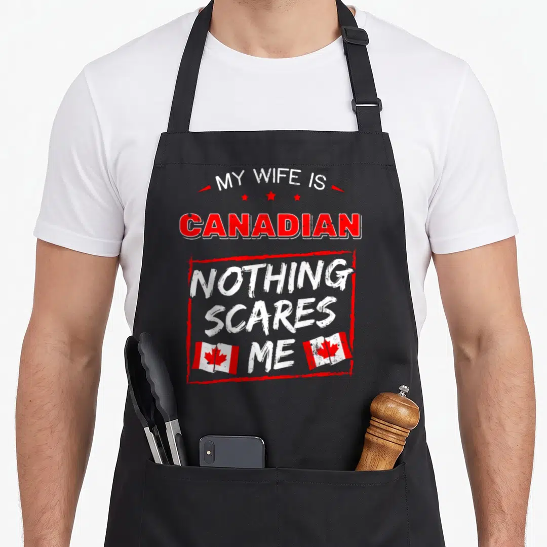 Canadian wife apron - Red and white stacked text reading My Wife Is Canadian Nothing Scares Me with three stars and two — shown on a black cotton canvas apron against a white background