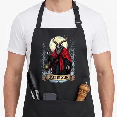 Gruss christmas apron - Krampus figure in red cloak holding lantern and staff under moon with banner text — shown on a black cotton canvas apron against a white background