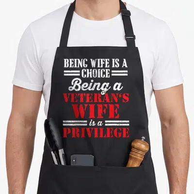 Privilege wife apron - Distressed white and red stacked text reading Being a veterans wife is a privilege — shown on a black cotton canvas apron against a white background