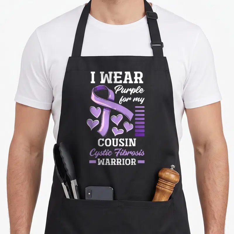 Cousin cystic fibrosis awareness apron - Purple ribbon five hearts white and purple text I wear for cousin warrior — shown on a black cotton canvas apron against a white background