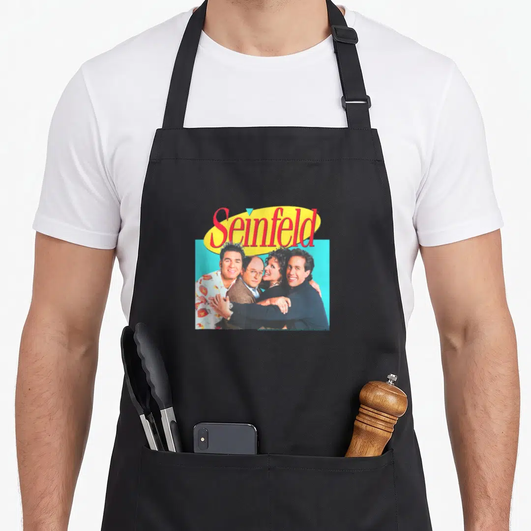 Hugging x apron - Seinfeld logo above photo of four cast members clustered on blue background — shown on a black cotton canvas apron against a white background