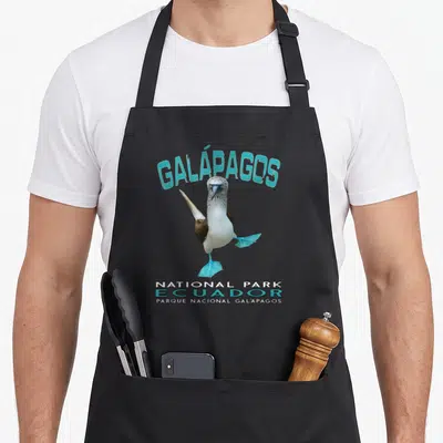 Galapago booby apron - Blue-footed booby with cyan feet and arched Galapagos text — shown on a black cotton canvas apron against a white background