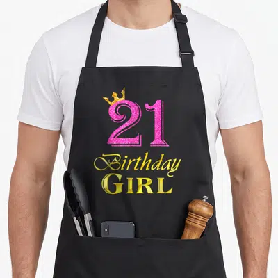 21st princess apron - Pink glitter number 21 with gold crown and stacked Birthday GIRL text — shown on a black cotton canvas apron against a white background
