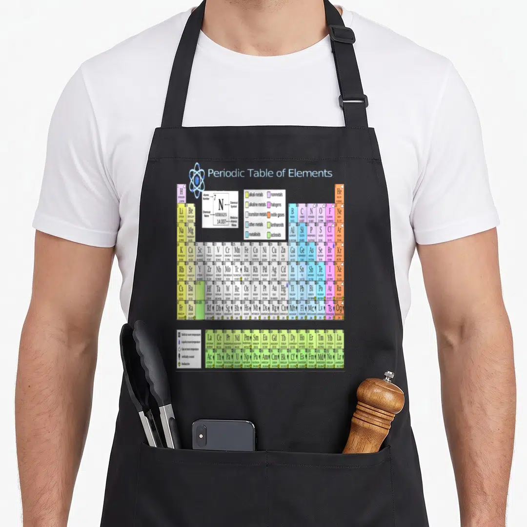 Periodic education apron - Colorful periodic table grid with atom diagram, legend, and state symbols at bottom left — shown on a black cotton canvas apron against a white background