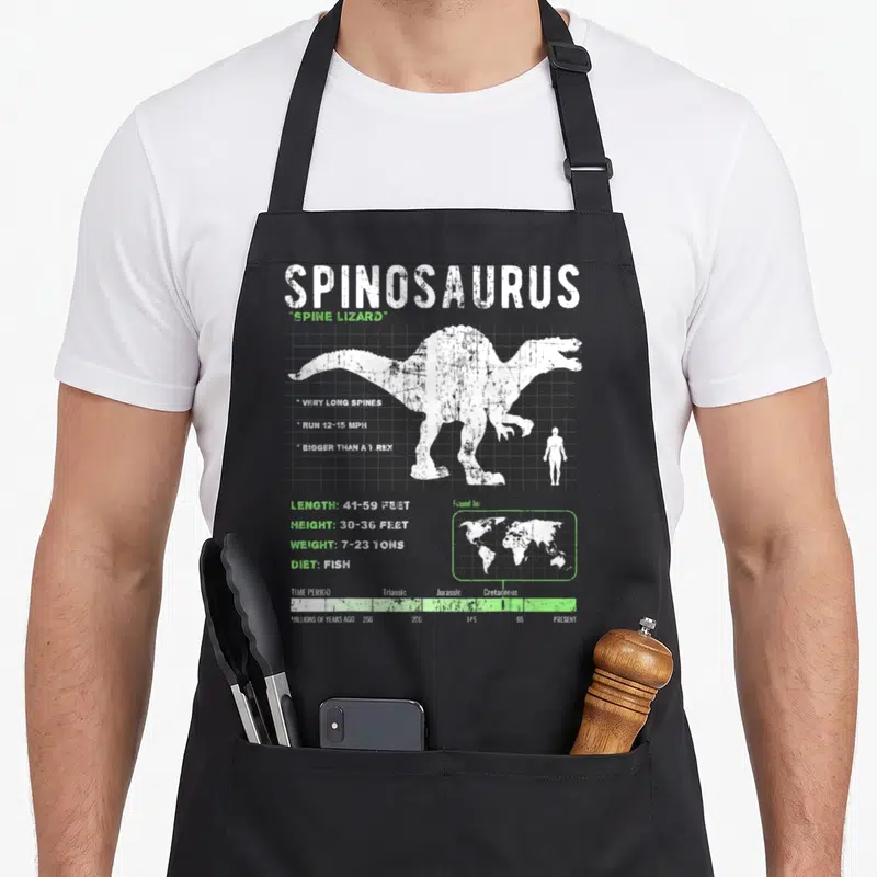 Fact dinosaur apron - White spinosaurus silhouette with stats and timeline on grey background — shown on a black cotton canvas apron against a white background