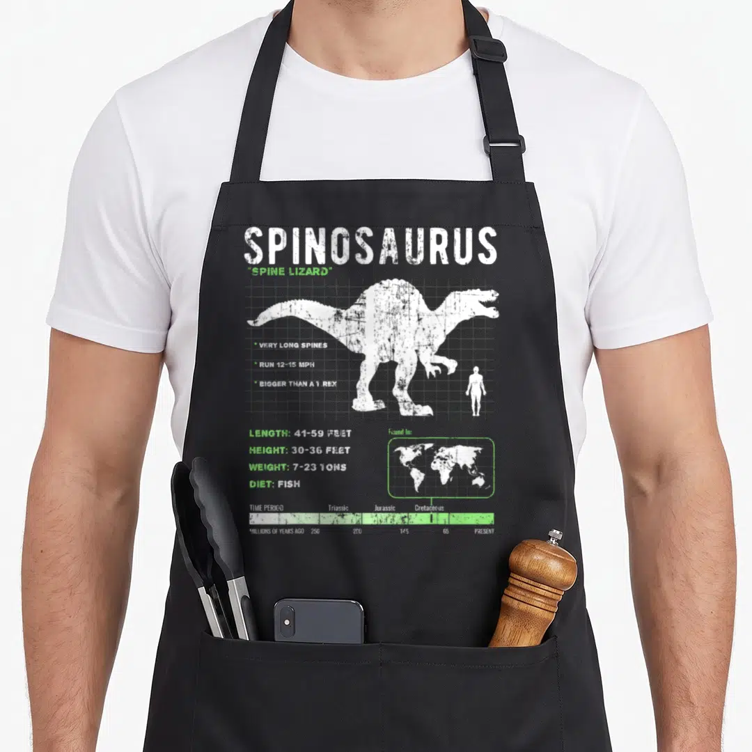 Fact dinosaur apron - White spinosaurus silhouette with stats and timeline on grey background — shown on a black cotton canvas apron against a white background