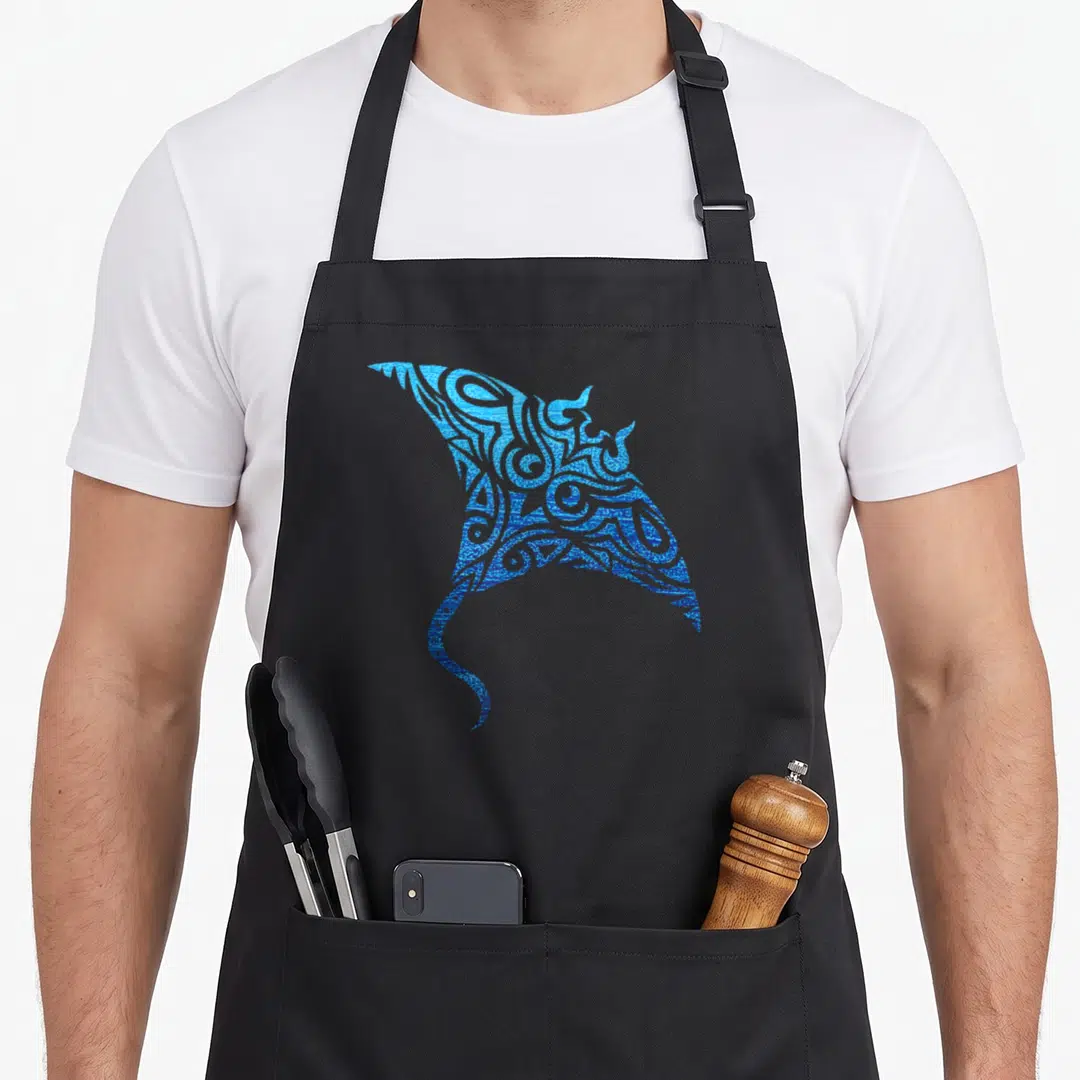Manta tattoo apron - Blue tribal line-art stingray with Polynesian swirl patterns centered on grey background — shown on a black cotton canvas apron against a white background