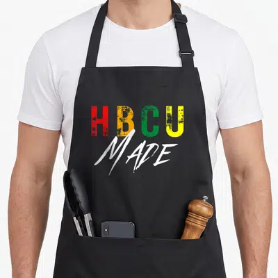 Student historical aprons - HBCU MADE text in red yellow green and white stacked typography — shown on a black cotton canvas apron against a white background