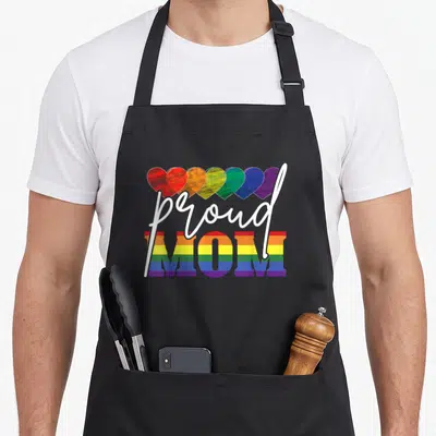 Lgbtq mother's day aprons - Seven rainbow hearts above white script proud and striped block MOM letters — shown on a black cotton canvas apron against a white background