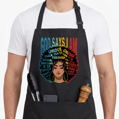Afro god says i am apron - Cartoon woman face with afro containing words UNIQUE CHOSEN FORGIVEN PSALM JOHN in blue — shown on a black cotton canvas apron against a white background