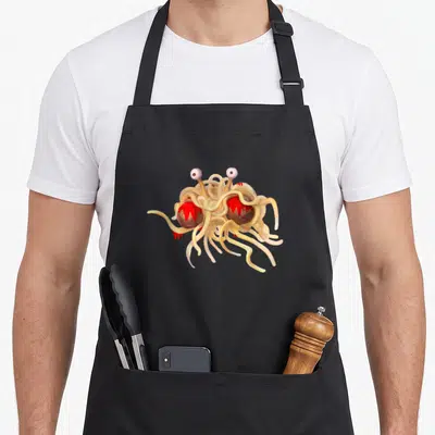 Atheist flying apron - Cartoon monster of noodles and meatballs with two eyes on stalks in beige, red, brown, and white — shown on a black cotton canvas apron against a white background