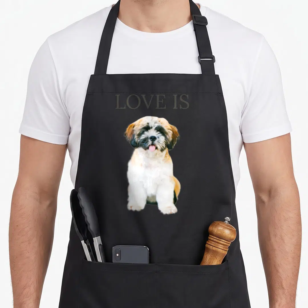 Pet puppy dog apron - LOVE IS text above a sitting Shih Tzu photo with white brown and black fur — shown on a black cotton canvas apron against a white background