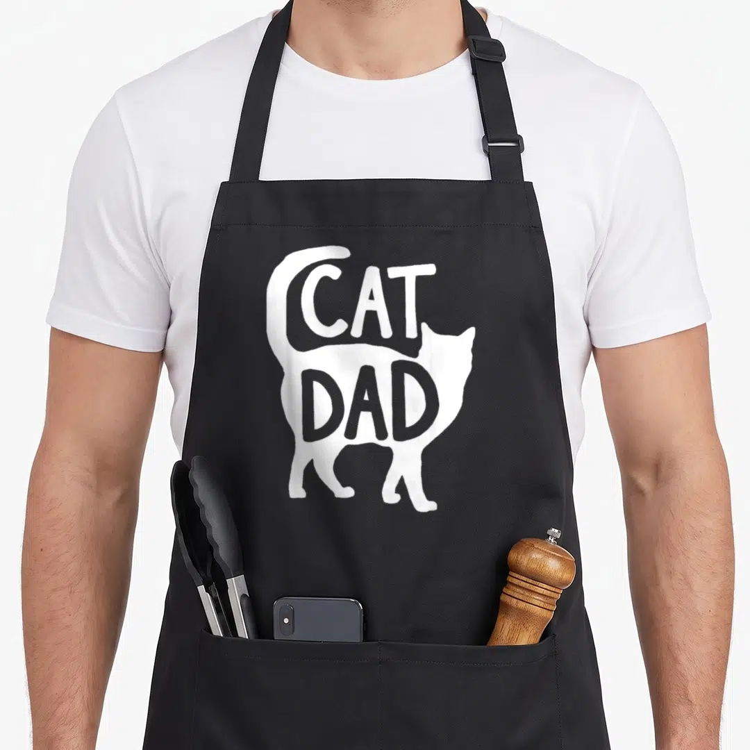 Cat grill daddy apron - White cat silhouette with CAT DAD text in negative space on black fabric — shown on a black cotton canvas apron against a white background