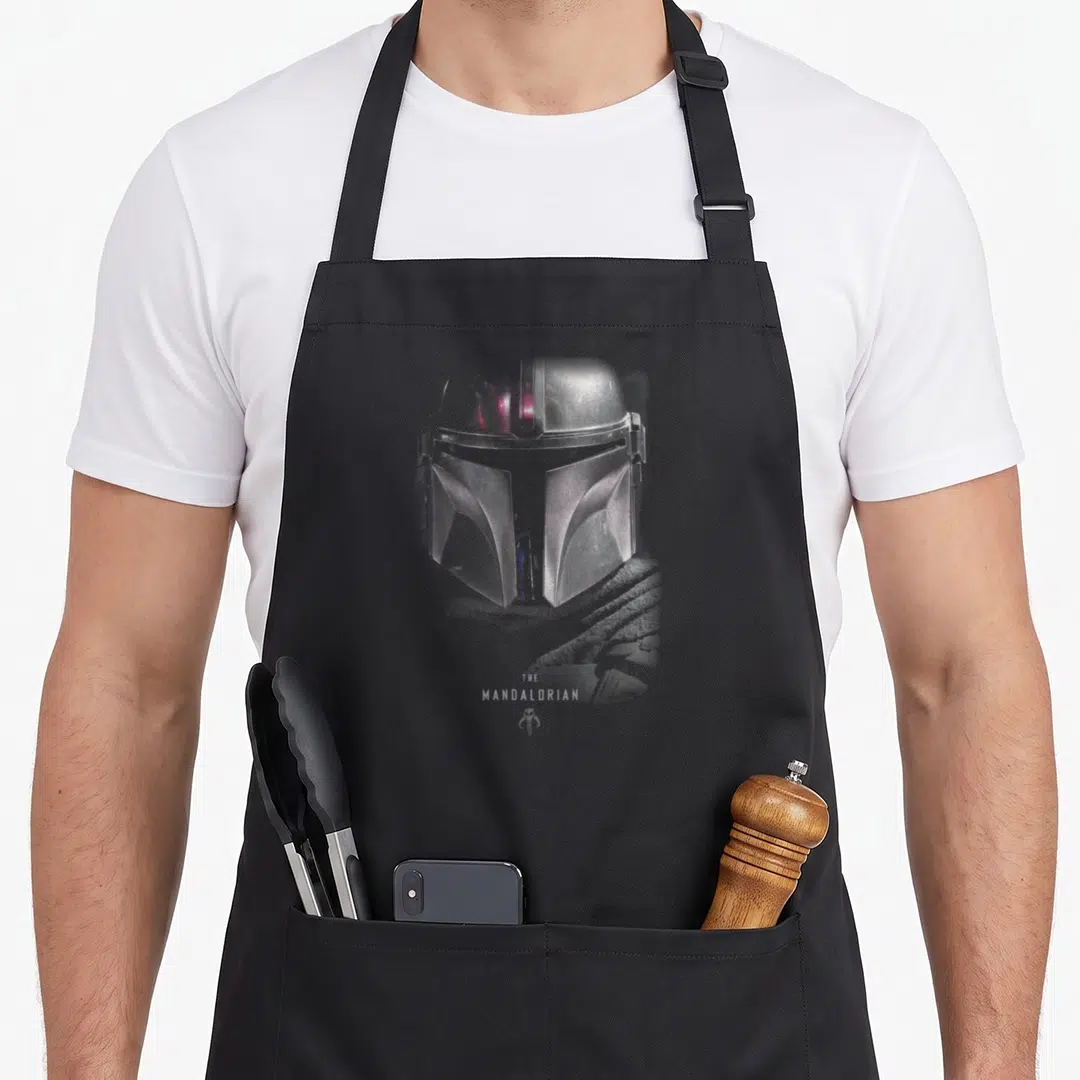 Dark wars new apron - Silver Mandalorian helmet print with THE MANDALORIAN text and small symbol below — shown on a black cotton canvas apron against a white background