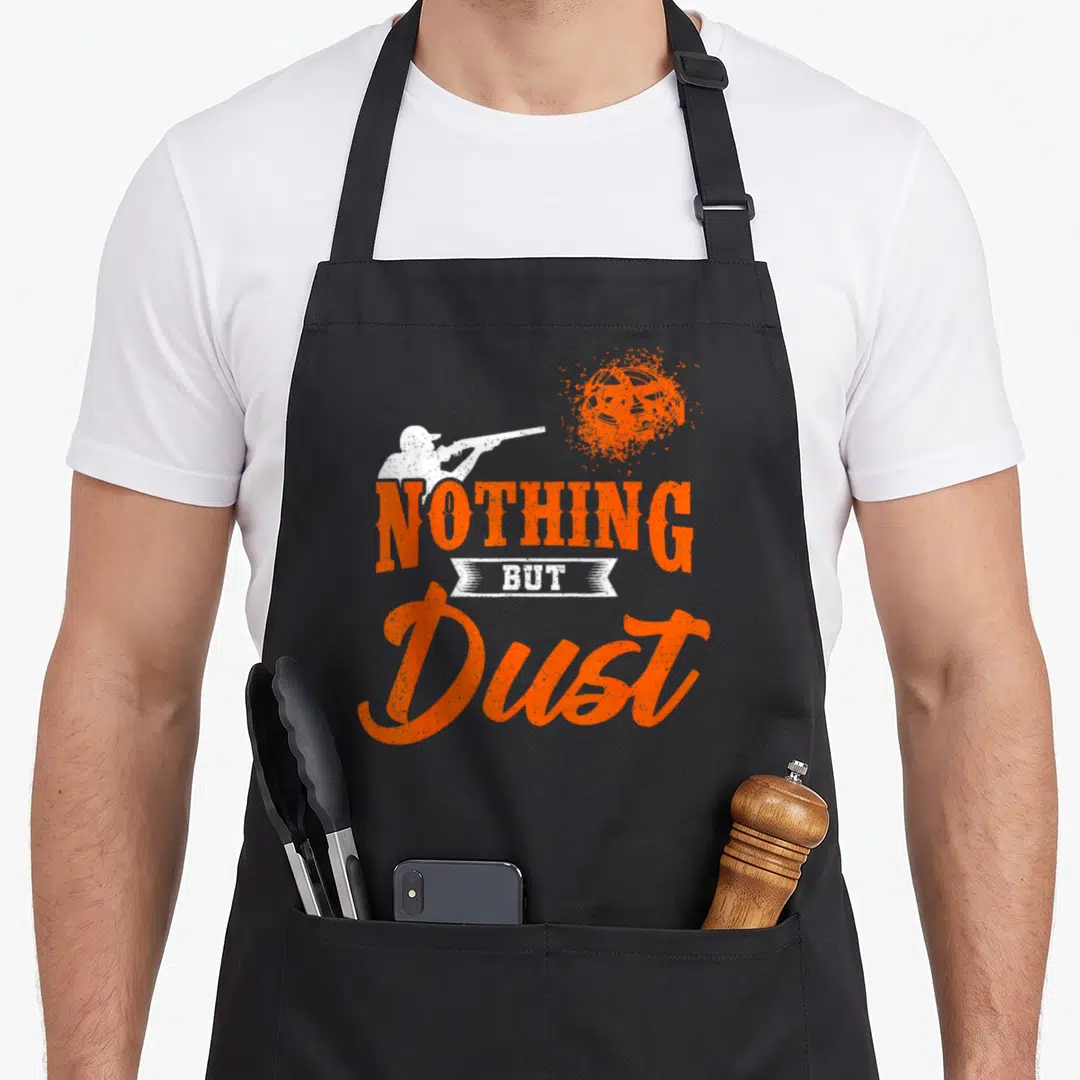 Clay nothing but apron - Shooter silhouette and shattered clay pigeon with NOTHING BUT Dust text in orange and white — shown on a black cotton canvas apron against a white background