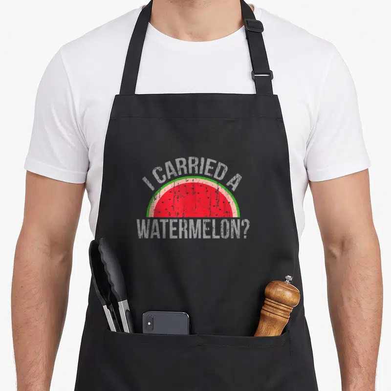 Carried watermelon apron - Half-slice watermelon with arched text I CARRIED A WATERMELON? in distressed grey — shown on a black cotton canvas apron against a white background