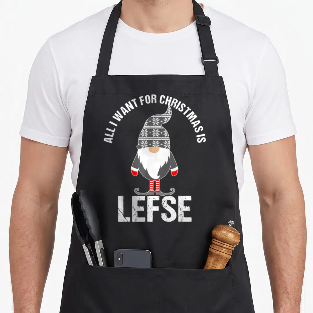 Tomte scandinavian aprons - Tomte gnome with grey snowflake hat and red striped socks under arched text and large LEFSE — shown on a black cotton canvas apron against a white background