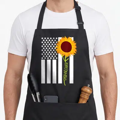 Motivational american flag apron - White flag graphic with orange sunflower and vertical DISPATCHER text on green stem — shown on a black cotton canvas apron against a white background