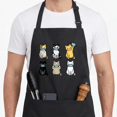 Face cat in an apron - Six cartoon cats in two rows wearing light blue face masks in orange, black, white, and grey — shown on a black cotton canvas apron against a white background