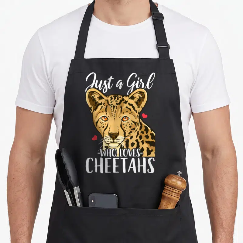 Funny cheetah apron - Realistic cheetah head with Just a Girl WHO LOVES CHEETAHS text and two red hearts — shown on a black cotton canvas apron against a white background