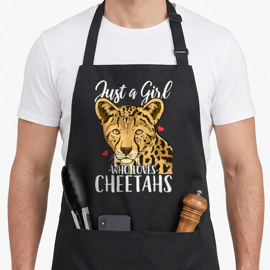 Funny cheetah apron - Realistic cheetah head with Just a Girl WHO LOVES CHEETAHS text and two red hearts — shown on a black cotton canvas apron against a white background