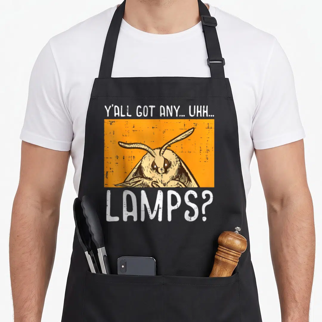 Yall meme apron - Cartoon moth in orange rectangle with white text YALL GOT LAMPS — shown on a black cotton canvas apron against a white background