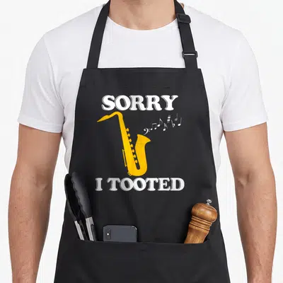 Tooted saxophone apron - Yellow saxophone illustration with white sorry i tooted text and musical notes — shown on a black cotton canvas apron against a white background