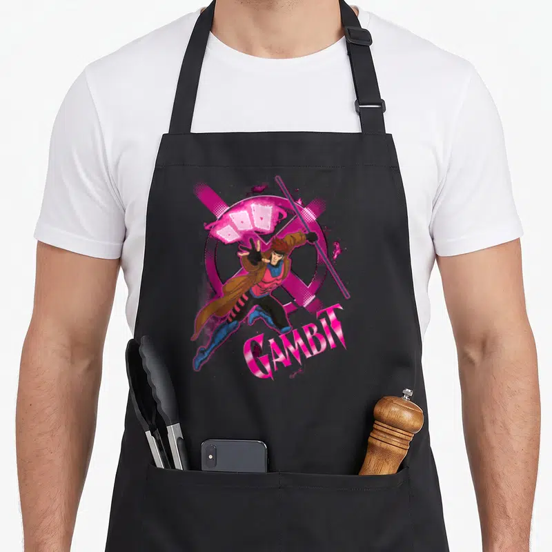 Throwing x apron - Gambit leaping with playing cards and X logo in pink purple brown blue cartoon style — shown on a black cotton canvas apron against a white background