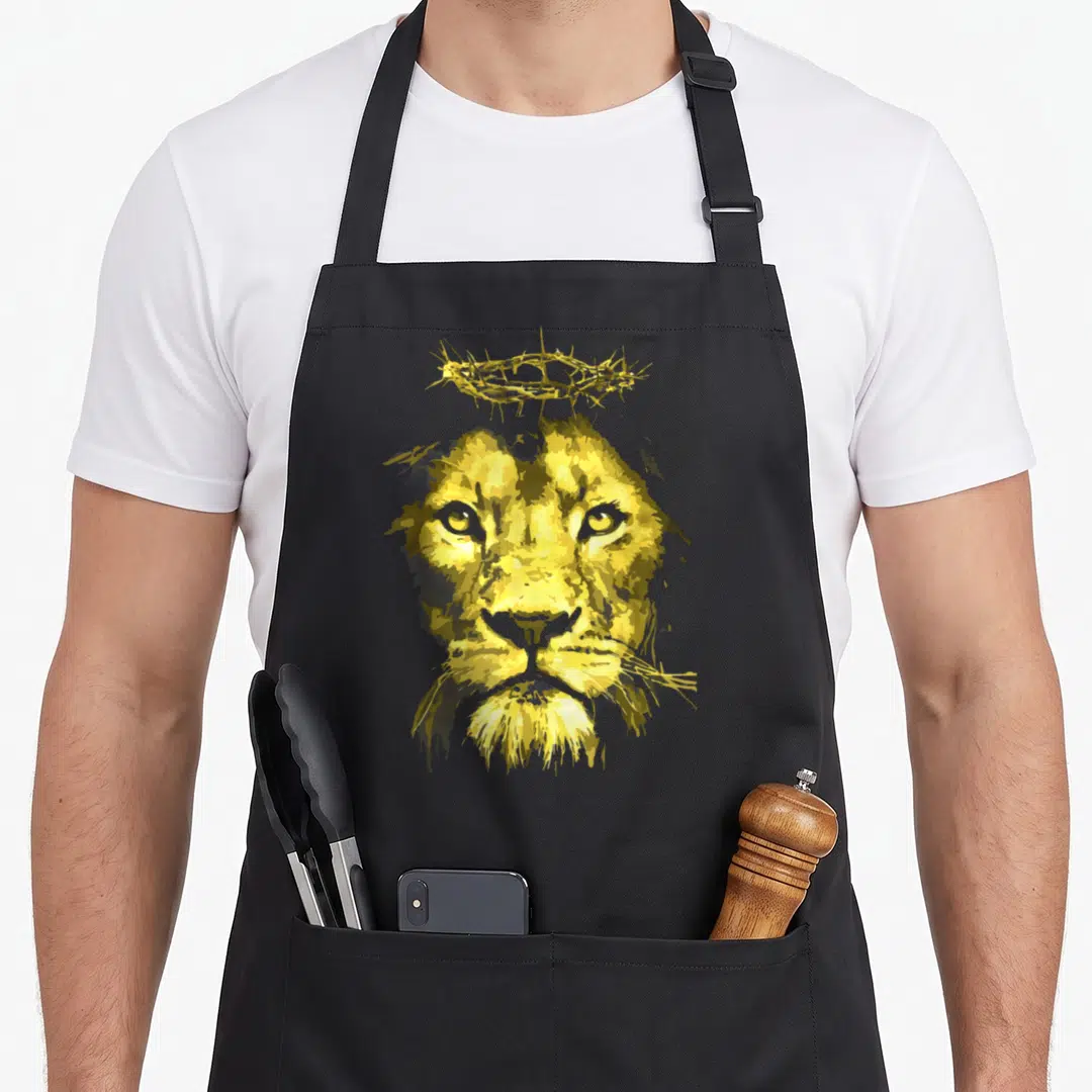 Funny judah lions apron - Yellow cartoon lion face with crown of thorns above head — shown on a black cotton canvas apron against a white background