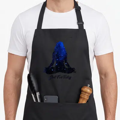 Today serenity apron - Galaxy silhouette of meditating woman with Just For Today text below — shown on a black cotton canvas apron against a white background