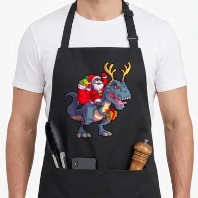Deer christmas santa apron - Cartoon Santa on blue-grey dinosaur holding orange gift box with antlers — shown on a black cotton canvas apron against a white background