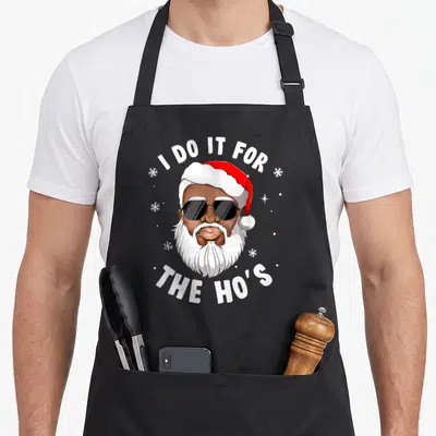 Hos african american aprons - Cartoon Santa with sunglasses and text I DO IT FOR THE HO'S on black background — shown on a black cotton canvas apron against a white background