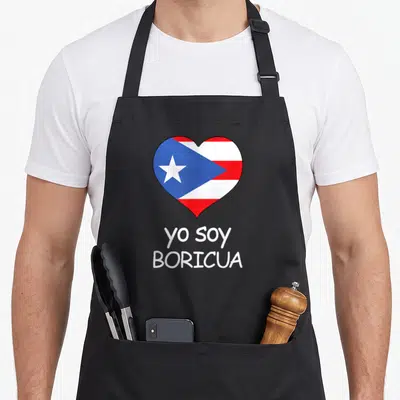 Soy spanish pride apron - Heart containing Puerto Rican flag above two lines of centered white text — shown on a black cotton canvas apron against a white background