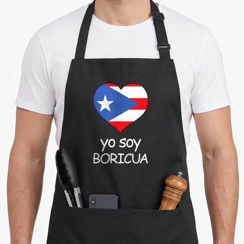Soy spanish pride apron - Heart containing Puerto Rican flag above two lines of centered white text — shown on a black cotton canvas apron against a white background