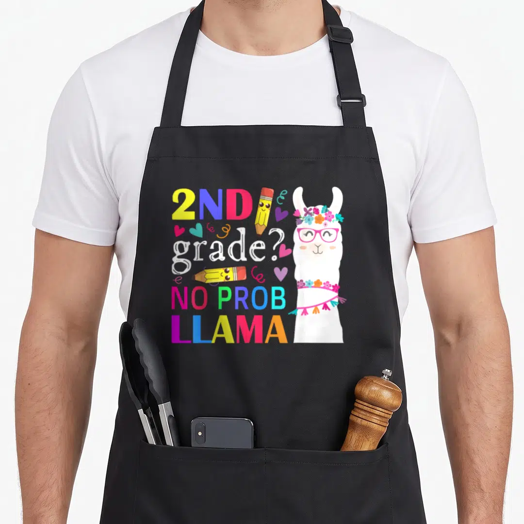 Prob 2nd apron - Cartoon llama with glasses and flower crown next to stacked text 2ND grade NO PROB LLAMA with two — shown on a black cotton canvas apron against a white background